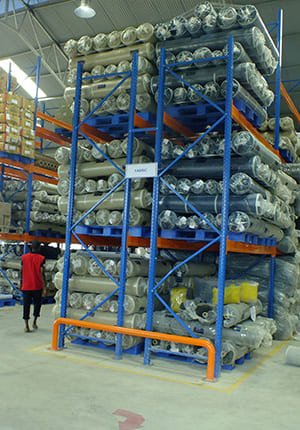 Warehouse scene with blue rackable plastic pallets supporting rolls of material on blue - framed racks, showcasing storage capabilities.