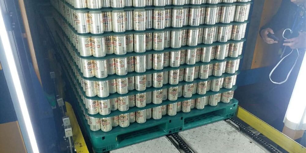 Rackable plastic pallets in green holding stacked cans in food and beverage packaging.