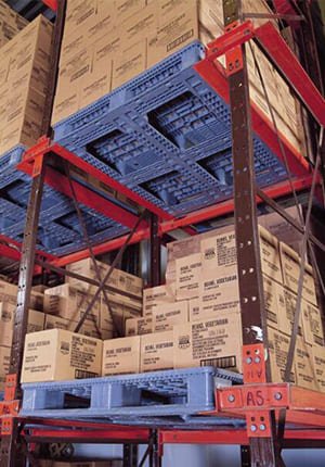 Storage area with blue plastic pallets holding cardboard boxes on red - framed racks, highlighting the use of plastic pallets in organized storage.