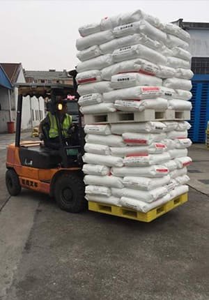 Forklift transporting a yellow industrial heavy - duty plastic pallet loaded with white bags, showcasing the heavy - lifting capacity of our plastic pallets.