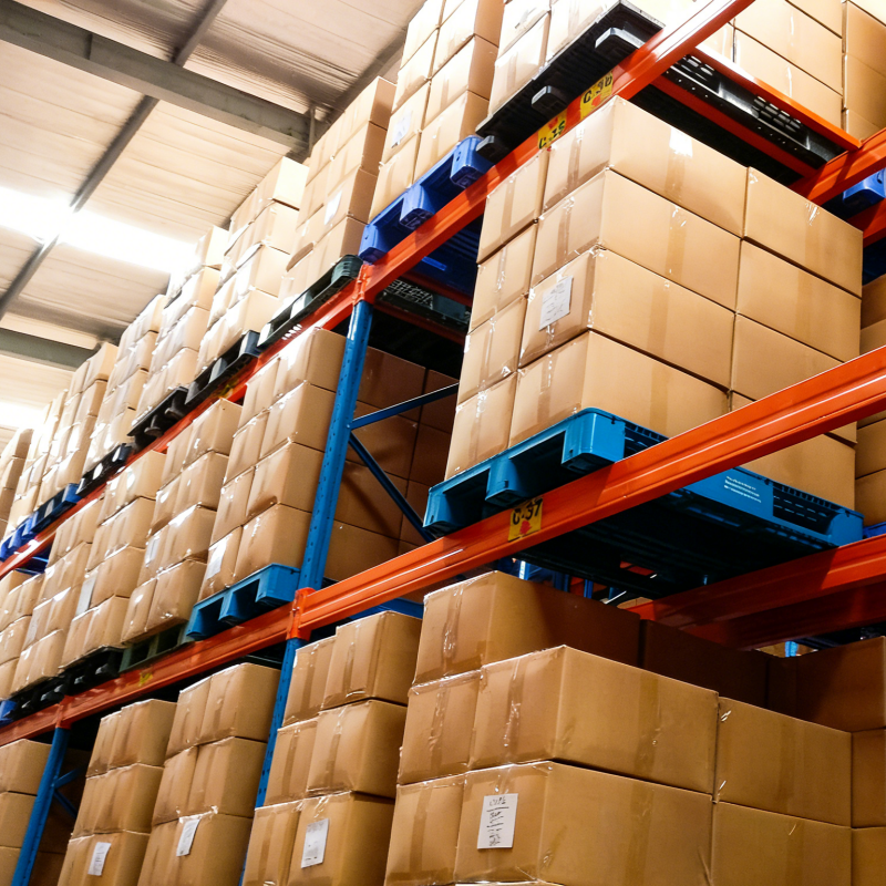 High-bay warehouse racking with blue plastic pallets holding stacked cardboard boxes